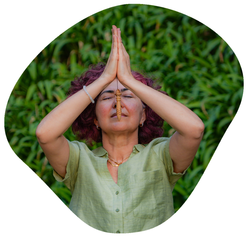 Mulher segurando um pêndulo de radiestesia com as mãos juntas acima da cabeça na natureza